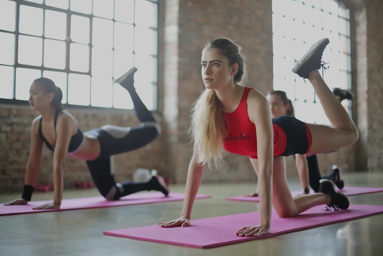 Group of women doing leg raises on yoga mats in a bright studio.