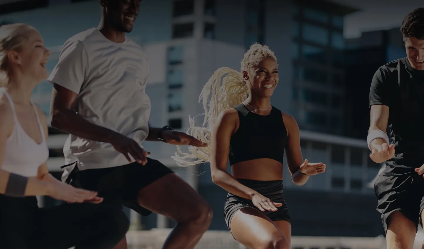 Group of people exercising outdoors in an urban setting, smiling and mid-motion during a group workout.